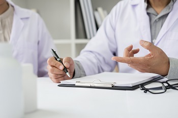 Two doctors discussing patient notes in an office pointing to a clipboard with paperwork as they make a diagnosis or decide on treatment.