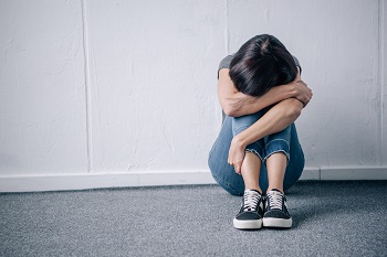 depressed lonely brunette woman sitting on floor at home with her head on her arms.