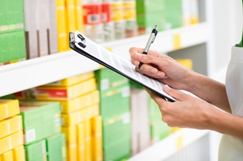 Supermarket clerk at work holding pen and clipboard with shelf on background, hands close-up.