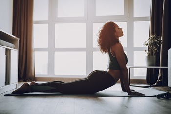 Woman flexing in a Yoga pose on a yoga mat on the floor.