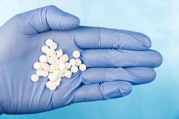 Blue-gloved hand pulls a handful of white pills