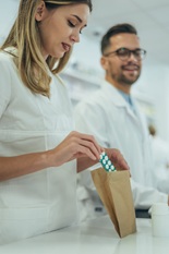 Close shot of a young female pharmacist packing drugs in a paper bag while working in a pharmacy